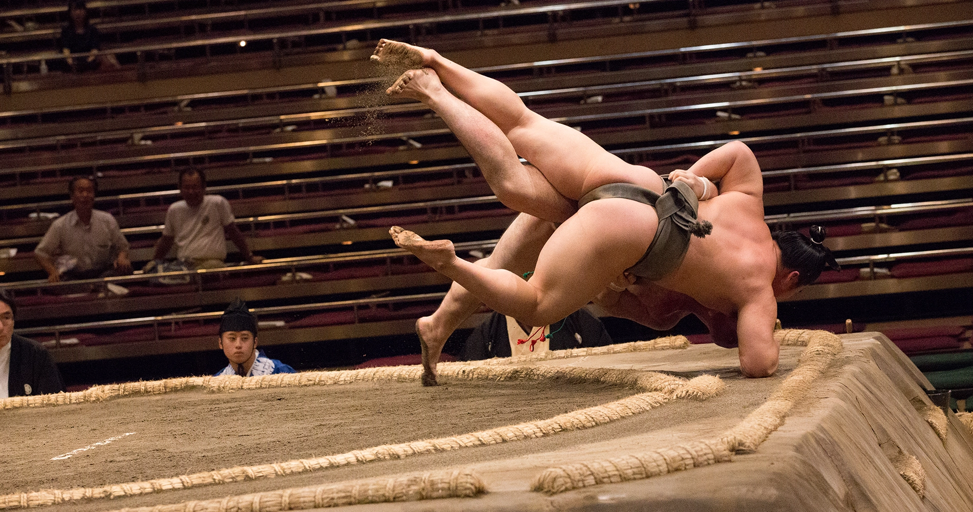Deux lutteurs de sumo en plein affrontement, l'un d'eux est déséquilibré et tombe sur le sol